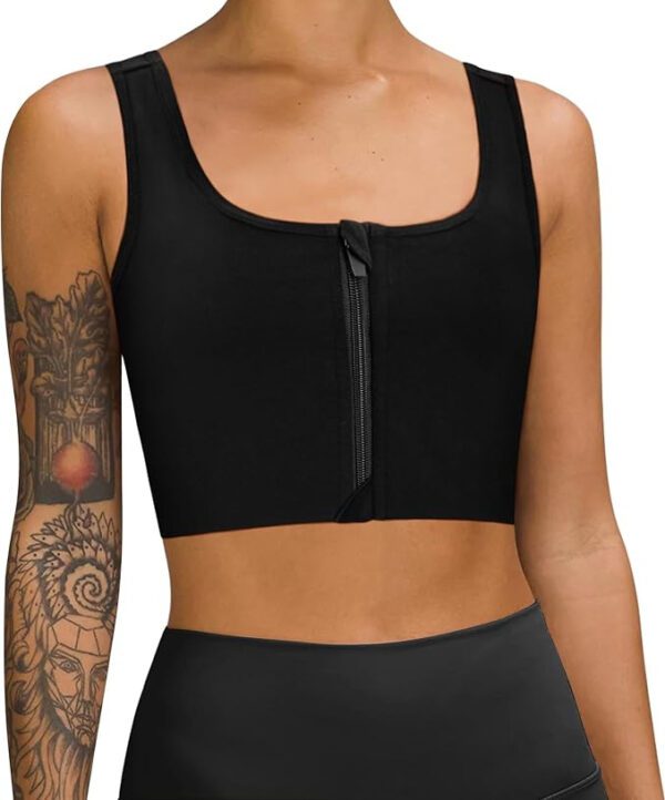 A person wearing a LEINIDINA black ftm chest binder with a front zippered closure and black high-waisted leggings. The individual boasts tattoos on their arms, showcasing intricate designs against the plain white background.