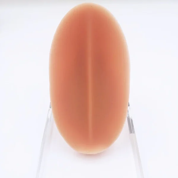 The back side of a smooth, oval-shaped, peach-colored object known as the MRIMIN Soft Packer is displayed upright against a white background, supported by a clear plastic stand.