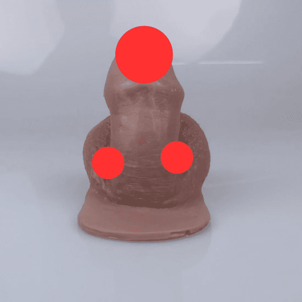 A silicone trans masculine packer is visible and sitting upright. Its smooth, brown surface showcases three red circular markers on the head, torso, and base for modesty. The backdrop remains a plain light grey.