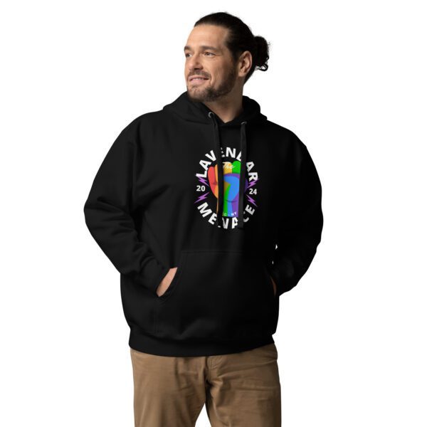 A person in a unisex hoodie with a colorful graphic featuring "Lavender Menace 2024" stands against a plain white background. They have hands in their pockets and are looking off to the side, wearing beige pants.